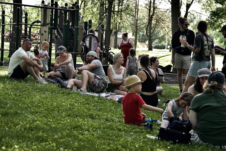 Individuals gather in park near playground. 